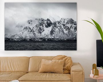 Black and white photo of low-hanging clouds and snow-capped mountains by Martijn Smeets