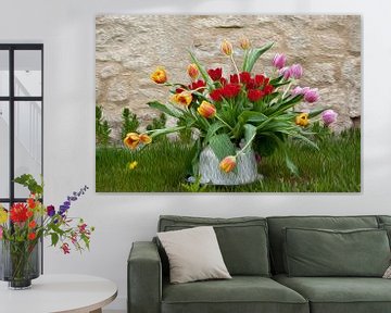 Tulpen in oude theepot op gras bij Franse muur