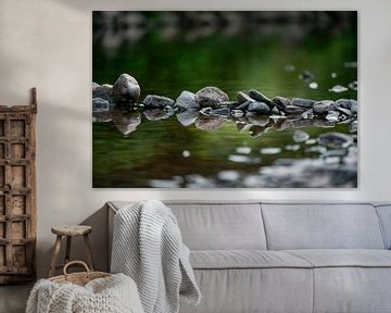 Reihe von Steinen mit einer schönen Spiegelung im Wasser in einem Bach mit grünem Hintergrund