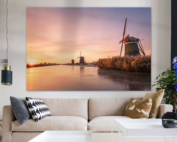 Three windmills along a frozen river at sunrise in winter