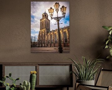 Lantaarnpaal voor de Lebuinuskerk met wolken boven de toren en zon in Deventer van Bart Ros