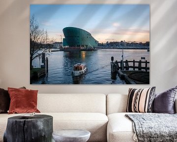 A boat sails in front of Nemo in Amsterdam near the Oosterdok with a light yellow cloudy sky