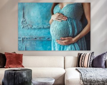Eine schwangere Frau hält ihren Bauch und lehnt sich an eine blaue Hauswand von Animaflora PicsStock