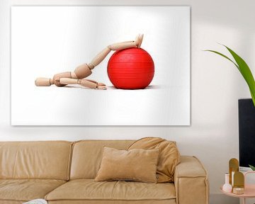 Holzpuppe macht eine physiotherapeutische Übung auf einem Gymnastikball