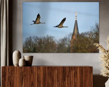 Kraanvogels vliegen bij een kerktoren boven een bos van Martin Köbsch