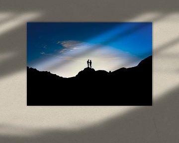 Silhouetten van twee mensen die op de top van een berg staan bij zonsondergang. Wout Kok One2expose von Wout Kok