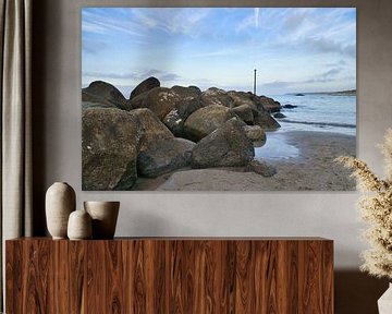 Stenen rotsblok steekt in zee op een zandstrand in Denemarken