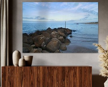 Stenen rotsblok steekt in zee op een zandstrand in Denemarken