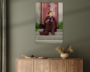 Chinese nun on steps in front of a burgundy door in Pingyao in China by Cindy Mulder