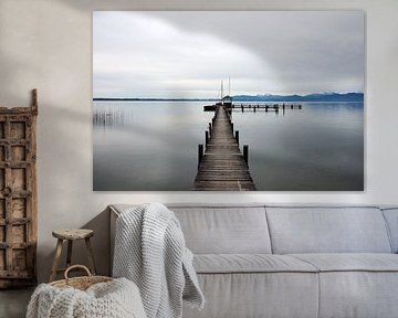 Serene image of a wooden jetty in Lake Chiemsee with a winter mountain landscape in the background.