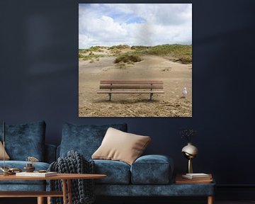 Een houten bank staat eenzaam op het strand, met alleen een meeuw als gezelschap. De duinen vormen een indrukwekkende achtergrond. van Marco Hoogma