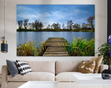 Het prachtige blauwe meer met bomen en de bewolkte lucht op de achtergrond en een houten pad dat er naartoe leidt van Andreas Völkel