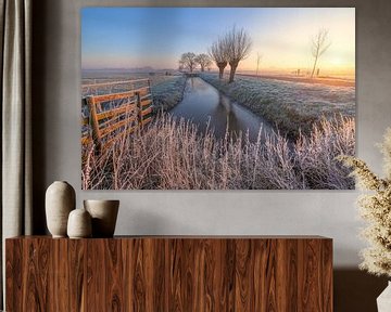 De eerste zonnestralen verlichten een klassiek Hollands polderlandschap tijdens zonsopkomst in de winter van Bas Meelker