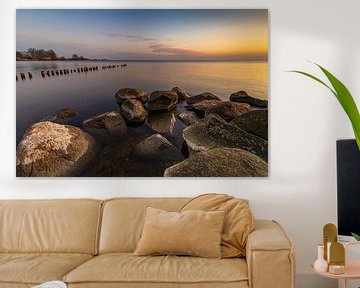 Gouden zonsopkomst aan het IJsselmeer met stenen en een golfbreker van houten paaltjes van Bram Lubbers