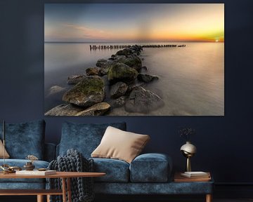 Een waterkering van grote stenen en paaltjes in het IJsselmeer bij zonsopkomst van Bram Lubbers