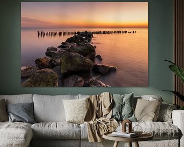 Een waterkering van grote stenen en paaltjes in het IJsselmeer bij een gouden zonsopkomst van Bram Lubbers