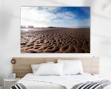 Vast zandstrand met stedelijke skyline onder heldere blauwe lucht.