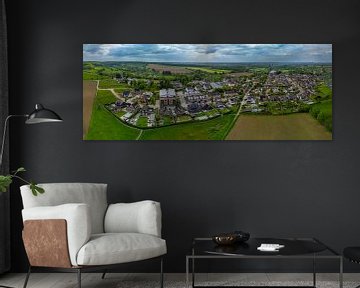 Panoramisch uitzicht op een vredig Limburgs dorp te midden van glooiende heuvels, groene velden en karakteristieke woningen onder een dramatisch wolkendek in de lente. van byphotographyms