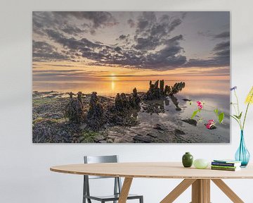 Ondergaande zon boven het Wad verlicht de wegtrekkende wolken en oude golfbreker van houten palen