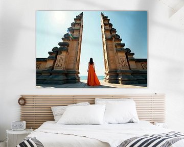 Femme en robe orange entre des piliers de pierre surplombant l'océan sur Markus Gann