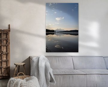A serene lake in Canada, surrounded by majestic mountains and lush green trees, under a blue sky during sunrise, with dew on the surface of the water and one boathouse in the foreground. The calm water reflects the landscape, creating a sense of symmetry and balance. The landscape exudes peace and serenity. by UMA Digital NL