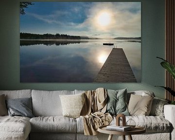 A wooden jetty on the lake in the morning mist, flooded with sunlight and a calm reflection. by Martin Köbsch