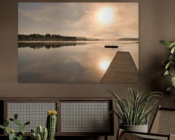 A wooden jetty on the lake in the morning mist, flooded with sunlight and a calm reflection. by Martin Köbsch