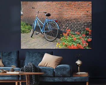 Blauwe fiets tegen muur met geraniums