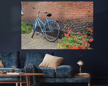 Blauwe fiets tegen muur met geraniums van Mariska van Vondelen