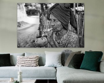 Old wrinkled woman smokes traditional cheroot cigar in front of her home in Baghan in Myanmar by Wout Kok