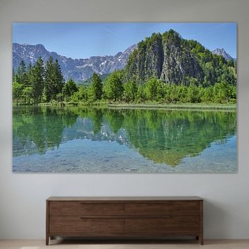 Ein Alpensee, in dem sich grüne Bäume und der strahlend blaue Himmel spiegeln von Tomherkules