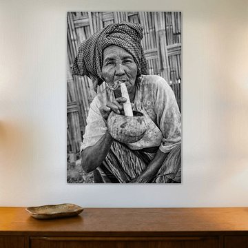 Old woman smokes traditional cheroot cigar in front of her home in Baghan in Myanmar by Wout Kok