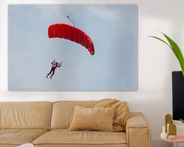 Parachutist aan een rode parachute tegen een blauwe lucht
