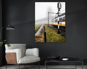 Een typische Nederlandse trein komt uit de mist en passeert een spoorwegsein. van Hans Post