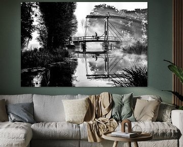 Lone newspaper delivery man cycles across a bridge in IJlst Friesland. One2expose Wout Kok Photograp by Wout Kok