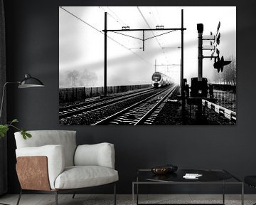 Zwart-wit foto van een Hollandse trein in mist bij spoorwegovergang van Hans Post