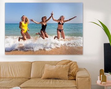 Drie meisjes springen op strand bij zee van Ben Schonewille