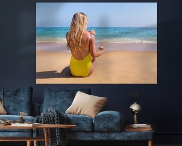 Young woman sitting on beach with sea smears herself with sunscreen sur Ben Schonewille