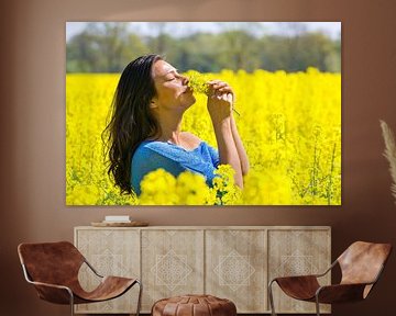 Vrouw ruikt aan bloemen in geel koolzaadveld van Ben Schonewille