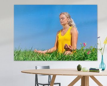 Jonge vrouw mediteert in gras met blauwe lucht van Ben Schonewille