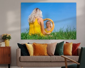 Young dutch woman sits with mirror in meadow with blue sky sur Ben Schonewille