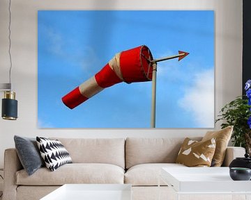 Roodwitte windwijzer in de volle wind met een blauwe lucht als achtergrond van Maarten Pietersma