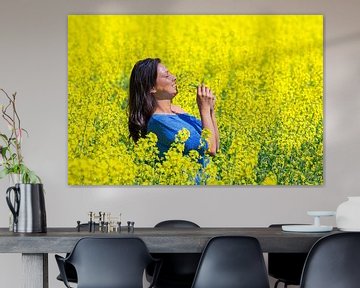 Jonge Columbiaanse vrouw ruikt gele bloemen in koolzaadveld van Ben Schonewille