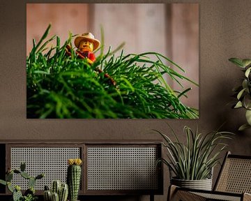 LEGO Minifigure with hat and red shirt is busy raking a plant in an industrial interior