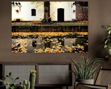 Zicht op een werfkelder aan de Nieuwegracht die vol ligt met herfstbladeren.