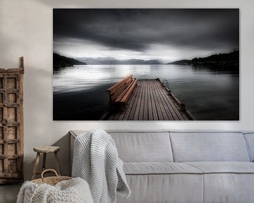 Een mystiek landschap in Noorwegen in zwart-wit met een meer. Een leeg bankje staat op een steiger b van Bas Meelker
