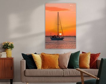 Een zeilbootje op zee met oranje lucht en ondergaande zon