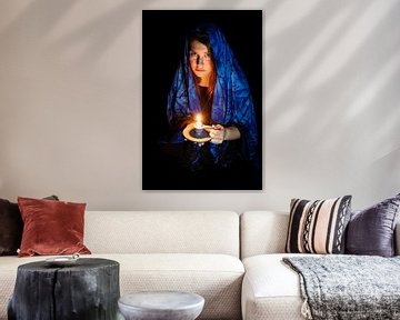 Sad young woman with candle and blue headscarf against black background by Hans-Jürgen Janda
