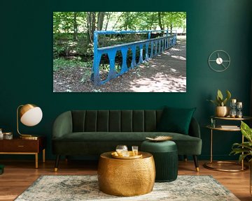 old blue metal bridge with wooden planks over a small river in a park with lots of greenery, trees a by ChrisWillemsen