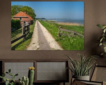 Een pad langs de dijk bij het waddenmeer, met een boerderij links van de weg van Anges van der Logt